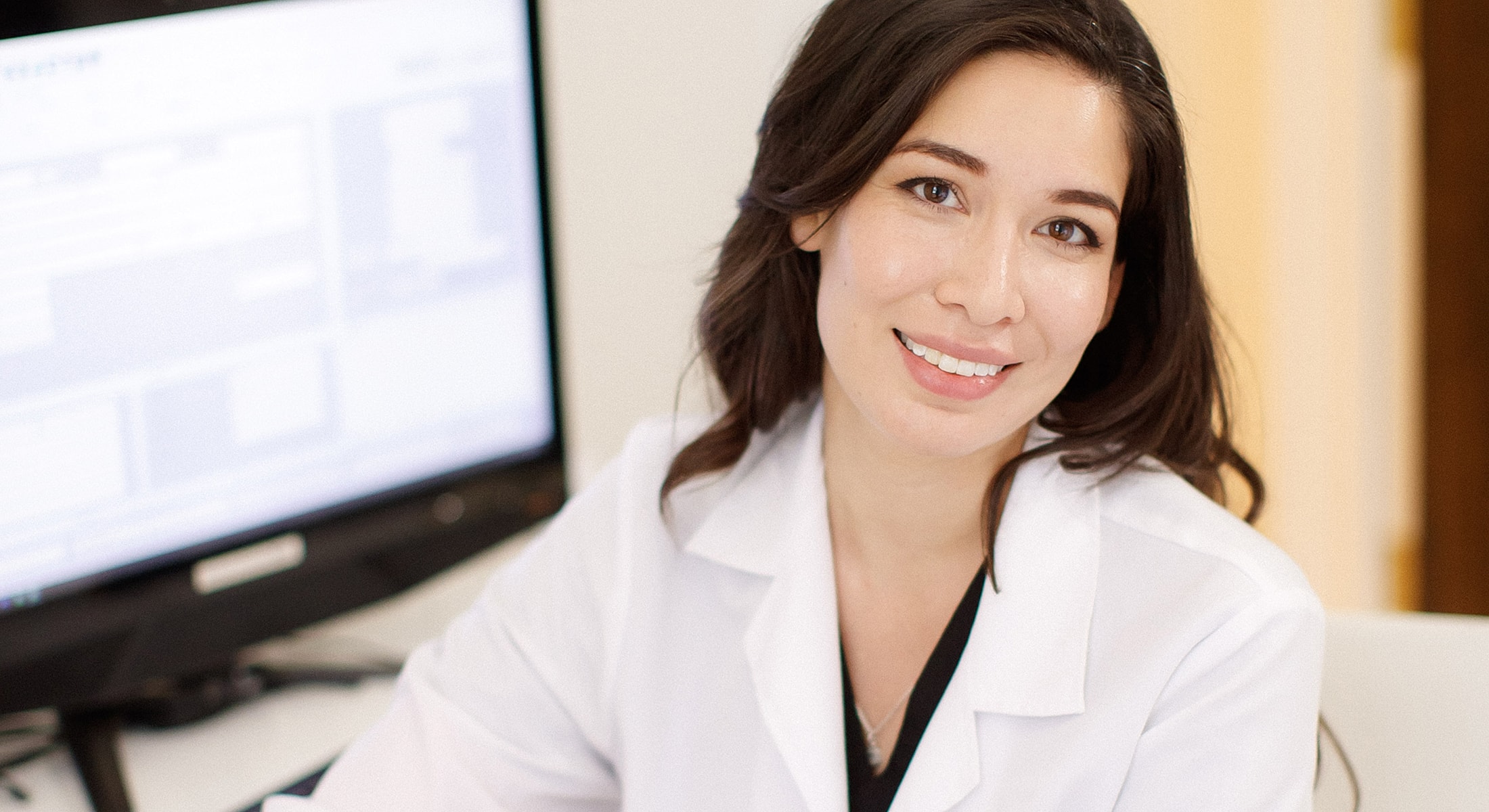 Smiling professional in a lab coat at desk.